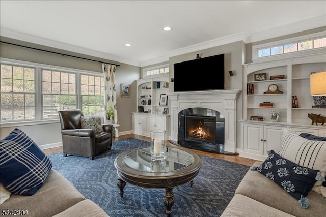 living room with a glass covered fireplace, ornamental molding, baseboards, and wood finished floors