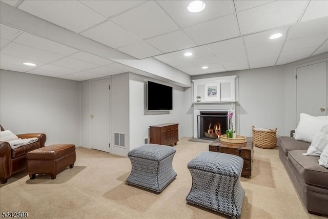 living area with light colored carpet, visible vents, a drop ceiling, and a lit fireplace