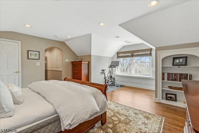 bedroom with vaulted ceiling, recessed lighting, wood finished floors, and arched walkways