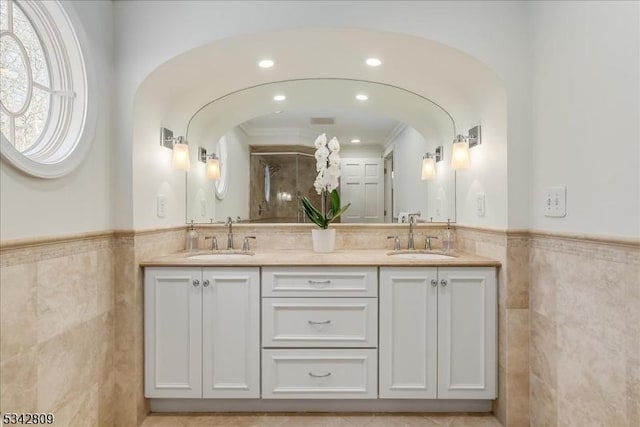 full bath featuring double vanity, tile walls, a wainscoted wall, and a sink