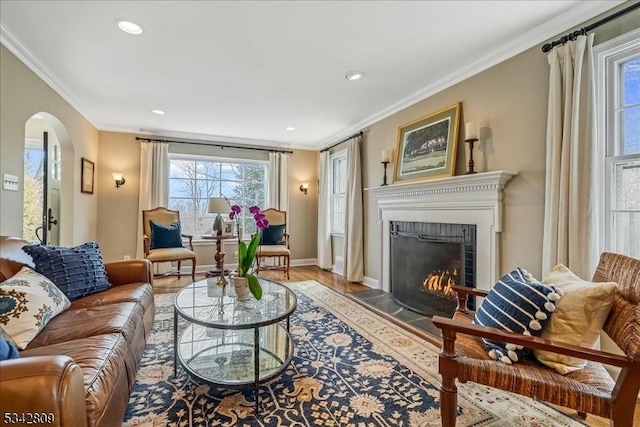 living area with a fireplace with flush hearth, ornamental molding, recessed lighting, arched walkways, and baseboards