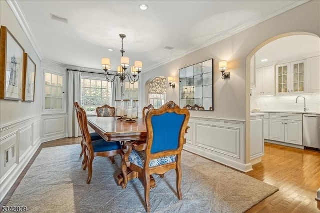 dining space featuring light wood finished floors, ornamental molding, an inviting chandelier, wainscoting, and a decorative wall