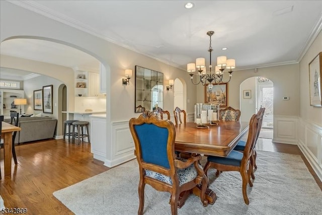 dining area featuring a wainscoted wall, a notable chandelier, wood finished floors, crown molding, and a decorative wall