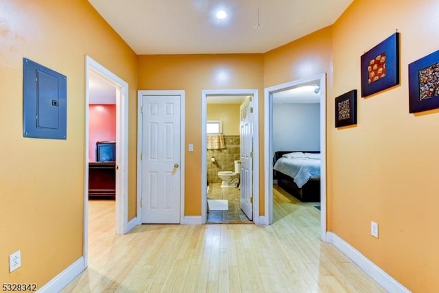 hallway with light wood finished floors, electric panel, and baseboards