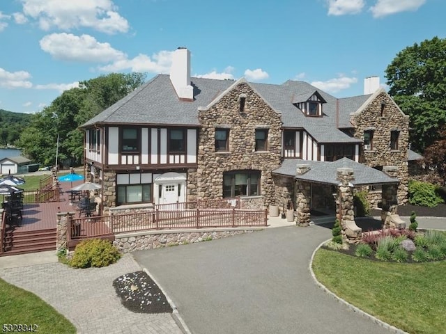 view of front of property with driveway, a chimney, stone siding, and fence