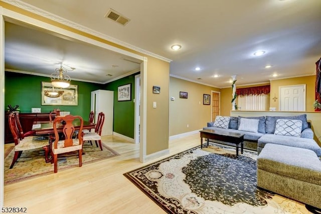 living room with ornamental molding, light wood-style flooring, visible vents, and baseboards