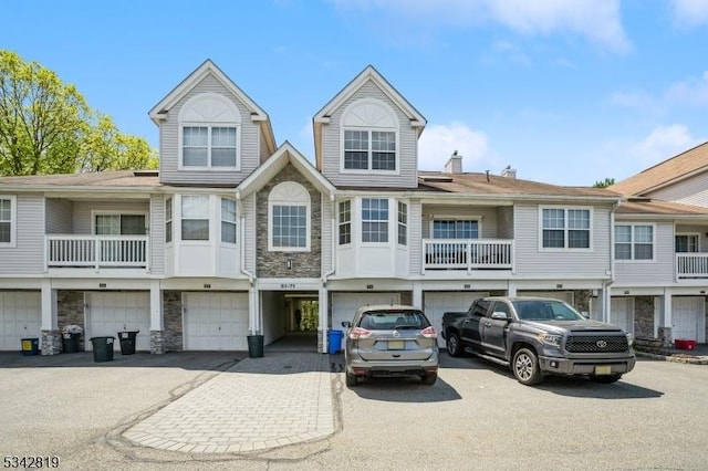 multi unit property featuring a garage, stone siding, and a chimney