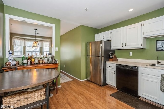 kitchen with a sink, black dishwasher, freestanding refrigerator, light wood-style floors, and white cabinets