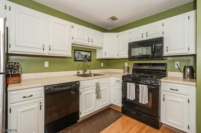 kitchen featuring a sink, visible vents, black appliances, and white cabinets