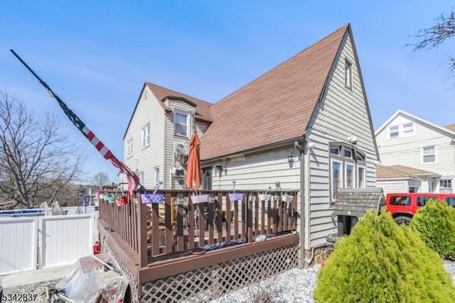 rear view of house featuring a wooden deck, roof with shingles, and fence