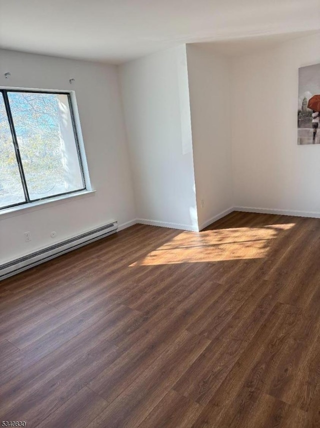 spare room featuring a baseboard heating unit, baseboards, and dark wood-style flooring