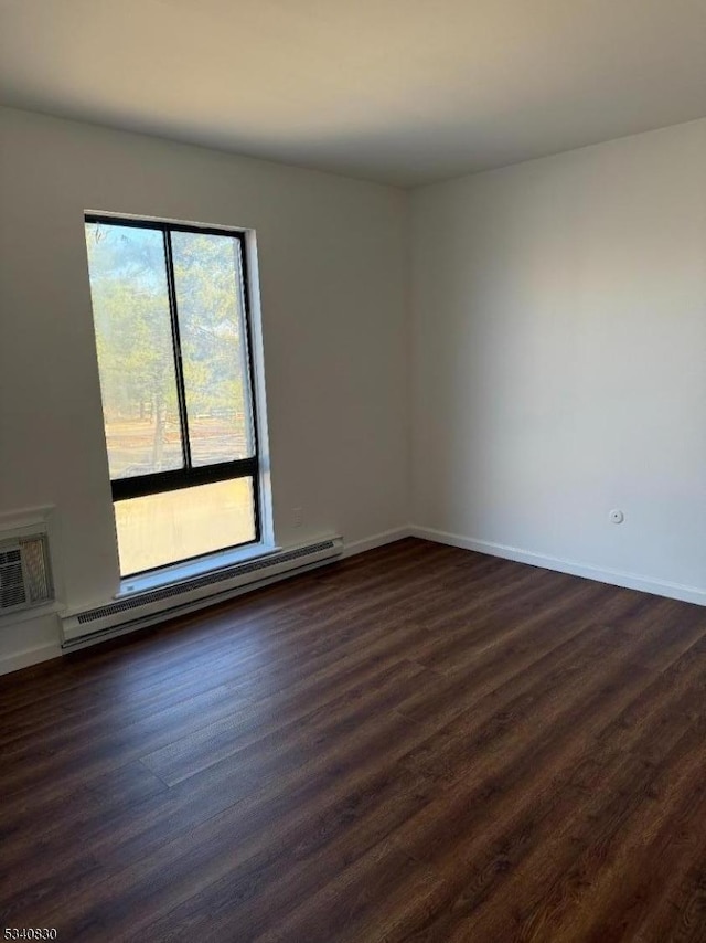 empty room featuring dark wood-style floors, baseboards, a wall mounted air conditioner, and a baseboard radiator