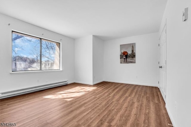 empty room with a baseboard heating unit, wood finished floors, and baseboards