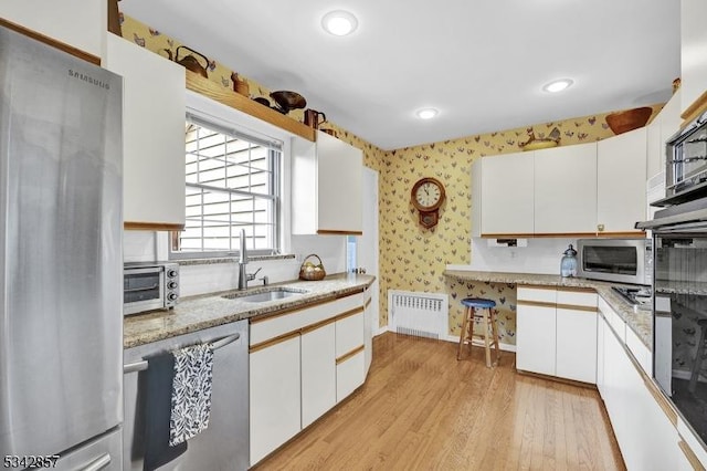 kitchen with stainless steel appliances, radiator, wallpapered walls, a sink, and light wood-style flooring