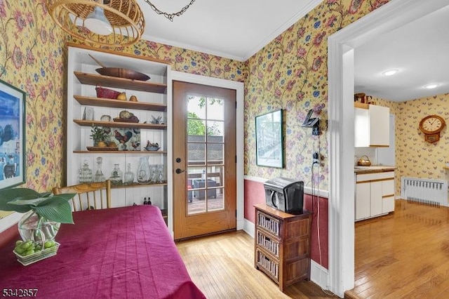 bedroom with radiator heating unit, wallpapered walls, light wood-style floors, crown molding, and access to outside