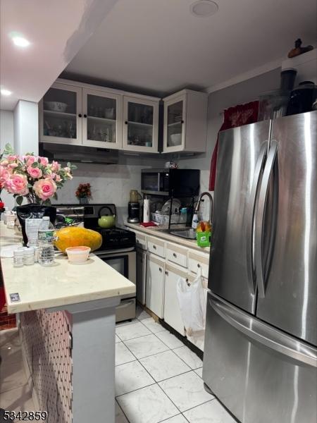 kitchen featuring stainless steel appliances, light countertops, glass insert cabinets, a sink, and a peninsula