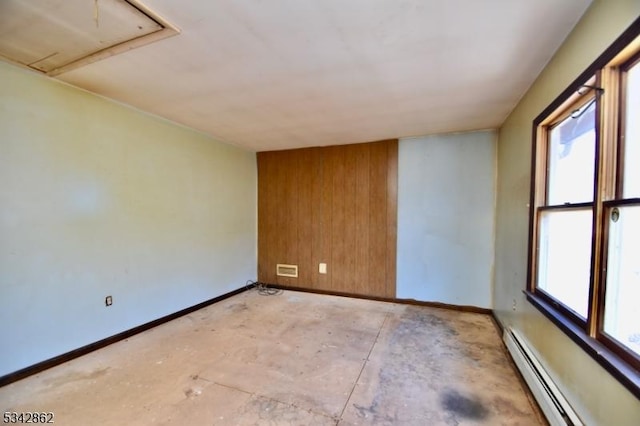 empty room with a baseboard heating unit, baseboards, wooden walls, and attic access