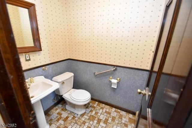 bathroom with a wainscoted wall, toilet, and wallpapered walls