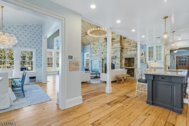 kitchen with a stone fireplace, wallpapered walls, light wood-style floors, and an inviting chandelier