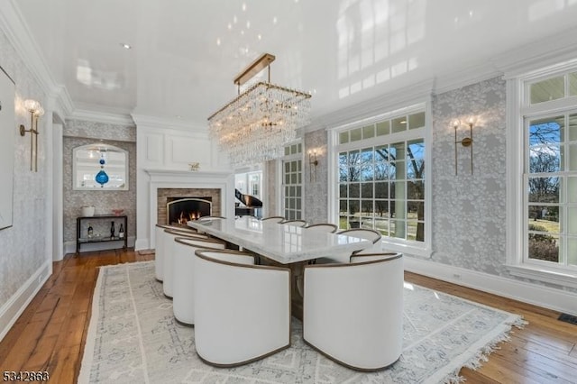 dining area with a warm lit fireplace, ornamental molding, and wallpapered walls