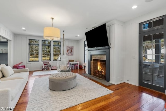 living room featuring recessed lighting, a fireplace with flush hearth, wood finished floors, and a decorative wall