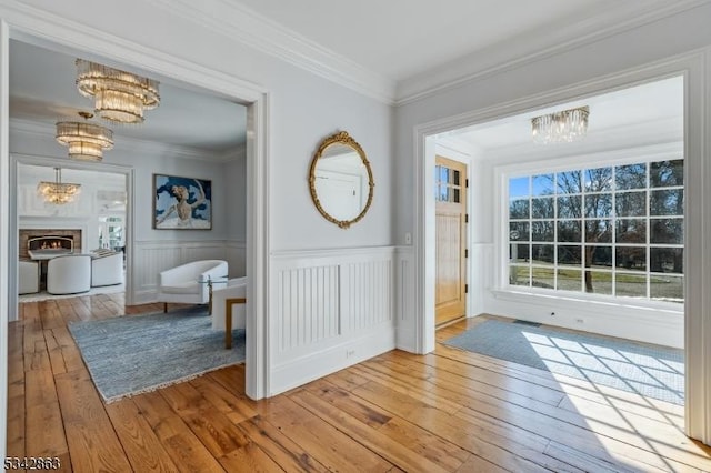 doorway to outside featuring a chandelier, a warm lit fireplace, light wood-type flooring, and crown molding