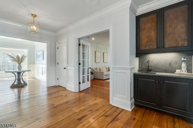 corridor featuring a notable chandelier, ornamental molding, a sink, light wood-style floors, and wainscoting