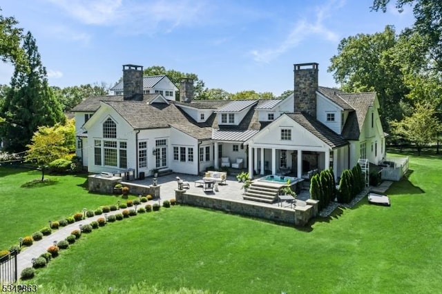 rear view of house with a standing seam roof, a lawn, a chimney, metal roof, and a patio