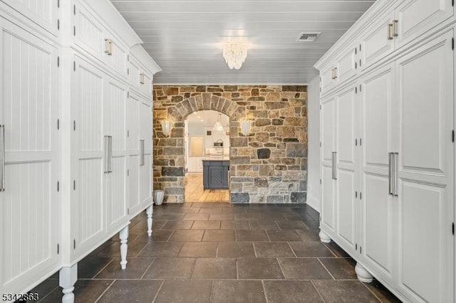 corridor featuring arched walkways, visible vents, stone finish flooring, and ornamental molding