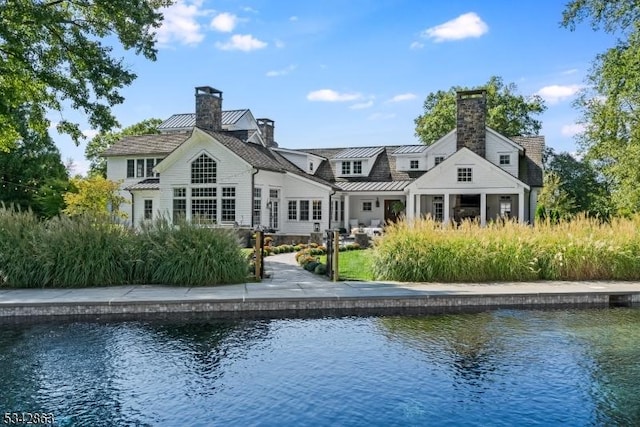 rear view of property with metal roof, a water view, a chimney, and a standing seam roof