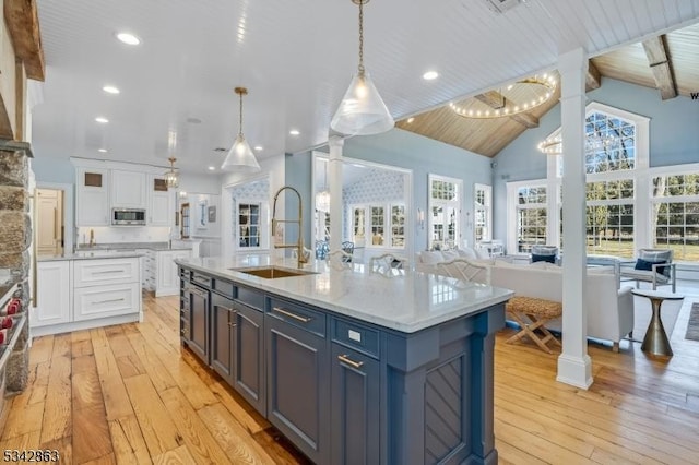 kitchen featuring a sink, open floor plan, white cabinetry, light wood-style floors, and decorative columns