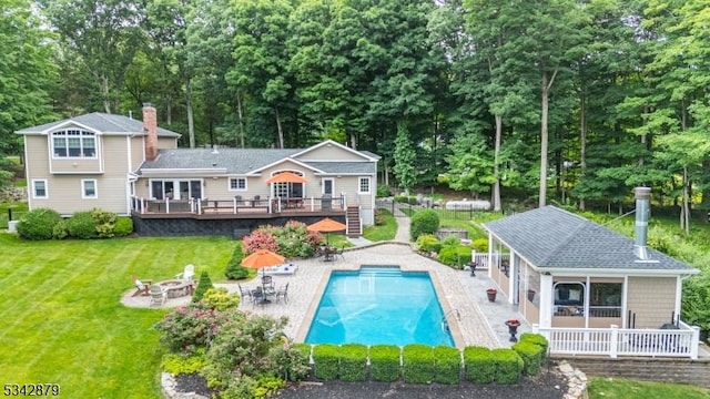 back of property featuring an outdoor fire pit, an outdoor pool, a deck, a patio area, and a lawn