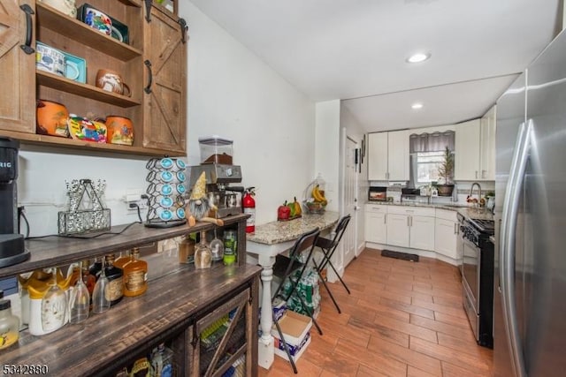 kitchen featuring a sink, white cabinetry, stainless steel appliances, light wood-style floors, and light stone countertops