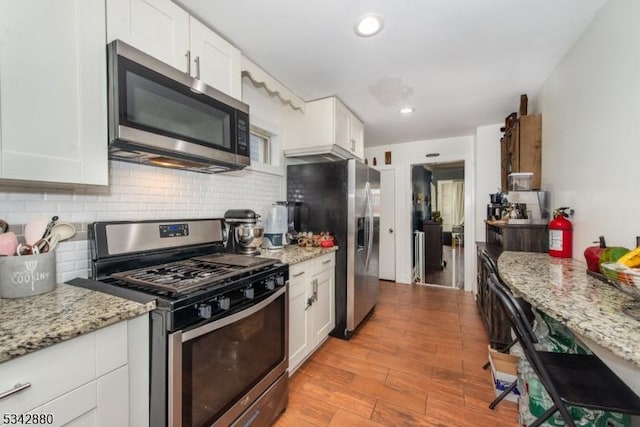 kitchen with light stone counters, light wood-style floors, appliances with stainless steel finishes, white cabinetry, and backsplash