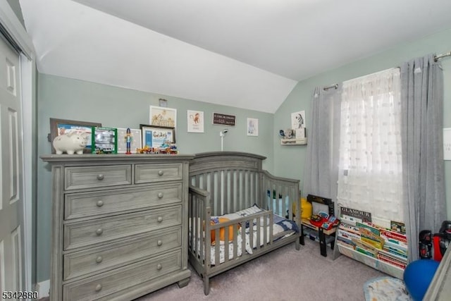 bedroom with a crib, lofted ceiling, and carpet floors