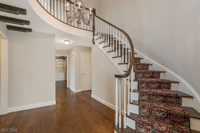 staircase with a chandelier, a towering ceiling, baseboards, and wood finished floors