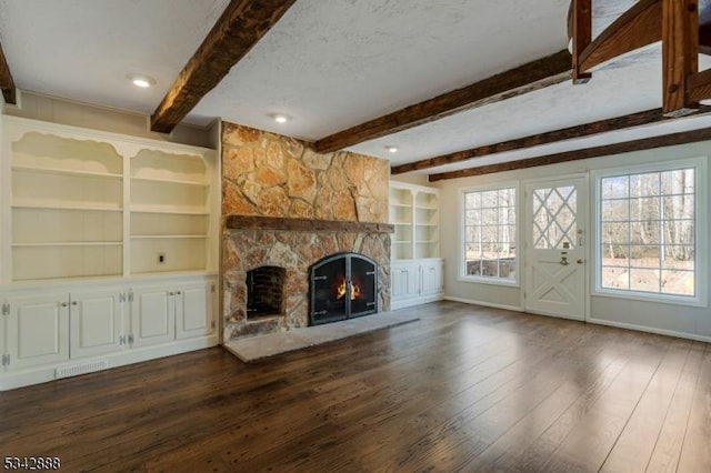 unfurnished living room with visible vents, beam ceiling, dark wood-style flooring, a stone fireplace, and a textured ceiling