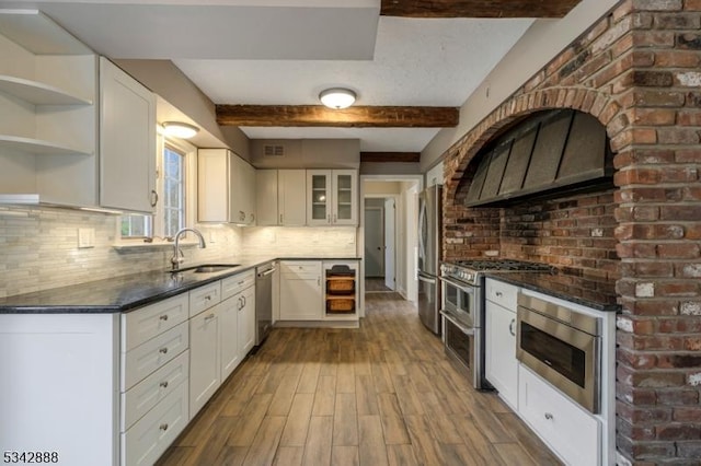 kitchen with stainless steel appliances, decorative backsplash, a sink, white cabinetry, and exhaust hood