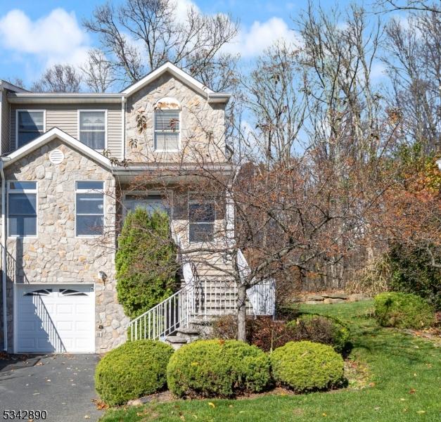 view of front of home with a garage, stone siding, stairs, and aphalt driveway