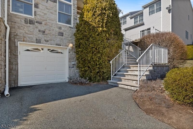 view of home's exterior with stairs, stone siding, driveway, and an attached garage