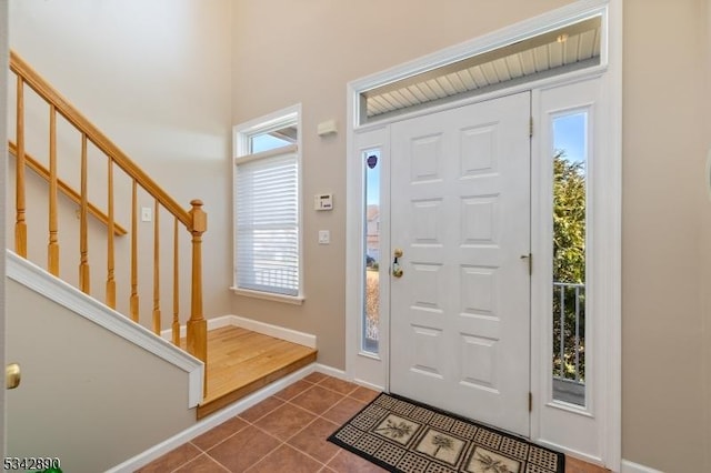 entryway with stairway, dark tile patterned floors, and baseboards