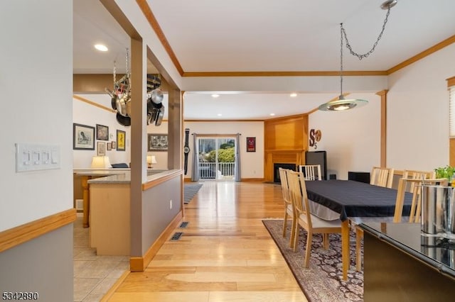 dining area with crown molding, baseboards, a large fireplace, and light wood-style floors