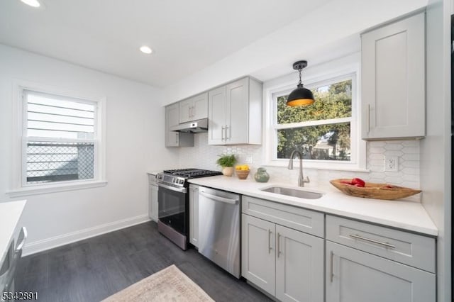 kitchen featuring gray cabinetry, baseboards, under cabinet range hood, appliances with stainless steel finishes, and a sink