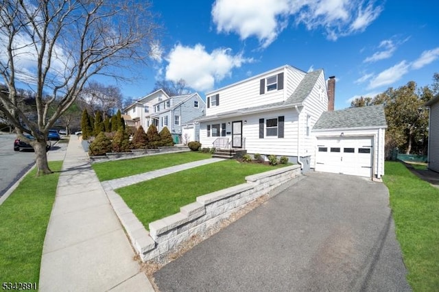 view of front of property featuring a front yard, roof with shingles, a chimney, driveway, and an attached garage