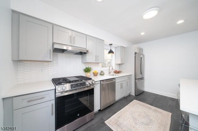 kitchen with backsplash, under cabinet range hood, light countertops, stainless steel appliances, and a sink