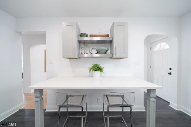 kitchen with a breakfast bar, open shelves, dark wood finished floors, arched walkways, and light countertops