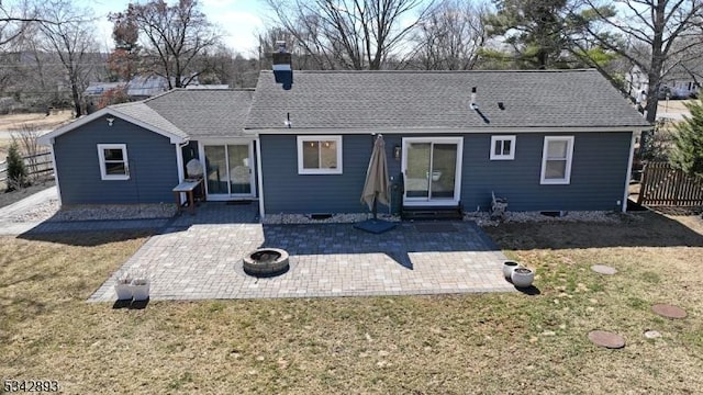 back of property with a yard, a shingled roof, a chimney, a fire pit, and a patio area