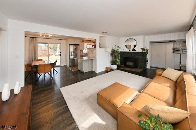 living area featuring a brick fireplace and dark wood-style floors