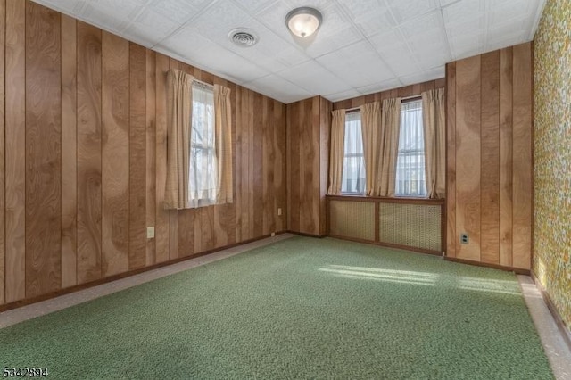 carpeted empty room with a wealth of natural light, visible vents, baseboards, and wooden walls