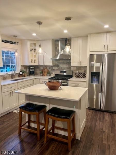 kitchen with tasteful backsplash, glass insert cabinets, wall chimney range hood, appliances with stainless steel finishes, and dark wood-style flooring